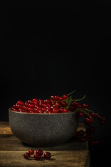 Red currants in a bowl on a black background. Berries from the village garden. Wooden vintage table