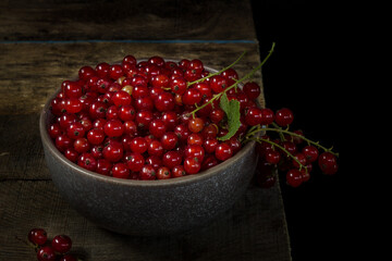 Red currants in a bowl on a black background. Berries from the village garden. Wooden vintage table