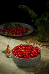 Red currants in a bowl on a black background. Berries from the village garden. Wooden vintage table