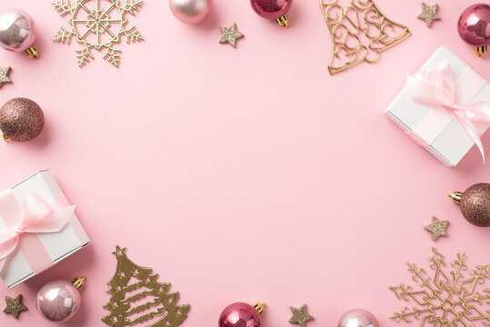Top view photo of christmas decorations pink balls gold bell pine snowflake shaped ornaments white gift boxes and shiny stars on isolated pastel pink background with blank space in the middle