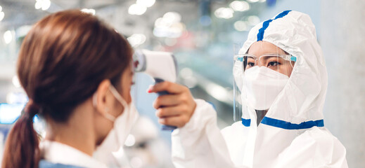 Doctor woman with protective suit use infrared forehead thermometer for check body temperature scan...