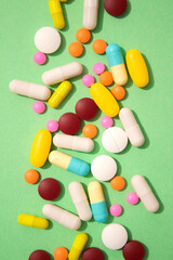 Vertical image of assorted multicolored medicine pills, capsules and tablets on green background. Immune system vitamins and supplemets. Various dietary bio supplements