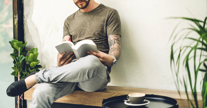 Handsome hipster man relaxing drink coffee and read the paper book work study and looking at page magazine while sitting on chair in cafe and restaurant