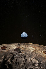 Footsteps on the moon surface, Earth rises above lunar horizon. Elements of this image furnished by NASA.