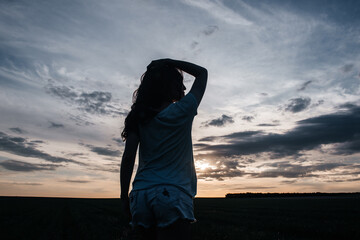 silhouette of a girl standing in a field at sunset and looking into the distance