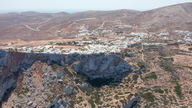 Aerial wide Panning shot Folegandros white Town on rocky hillside and Mountain cliffs
