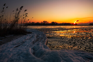Natural Winter landscape on seashore during sunset. Ice and sunset sky.