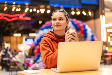 Fototapeta premium Alternative girl with white braids using a computer in a shopping center, sending an email