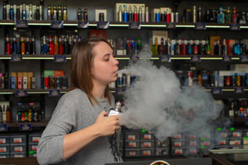 Young pretty caucasian woman with brown hair smoke an electronic cigarette at the vape shop. Vaping...
