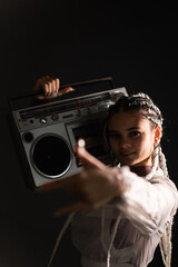 Portrait of a young girl with white braids with a boombox on her shoulders, black background, 80s style, retro photography, vertical photo