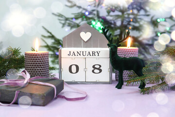 Calendar for January 8: the name of the month in English, numbers 0 and 8, burning candles, a gift tied with a purple ribbon, a figurine of a deer against the background of a festive tree, bokeh