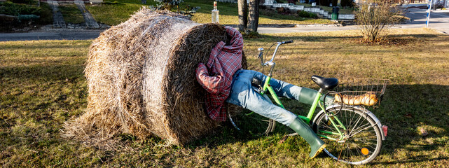 A drunk rural cyclist crashes into a stack of straw, humorously arranged decoration with a puppet in the countryside