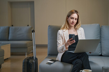 Young lady dialing number on smartphone in hotel lobby