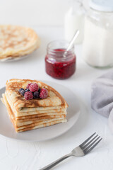 Thin pancakes with berries. White background. Nice breakfast. Pancakes with sour cream and raspberry jam.