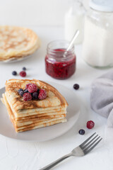 Thin pancakes with berries. White background. Nice breakfast. Pancakes with sour cream and raspberry jam.