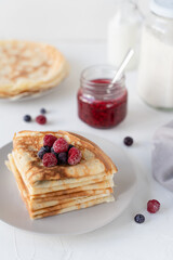 Thin pancakes with berries. White background. Nice breakfast. Pancakes with sour cream and raspberry jam.