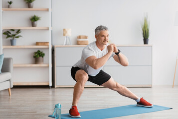 Home serobics. Mature man doing lunges exercises on mat in living room, enjoying domestic fitness...