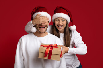 Xmas Surprise. Happy Young Woman Holding Gift Box And Covering Boyfriend's Eyes