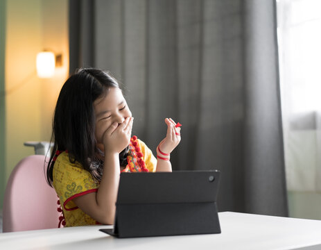 asian child enjoy learning on computer tablet or kid girl student laughing hand close mouth on back to school by video call or person happy fun learn from home by studying online class on pad and desk