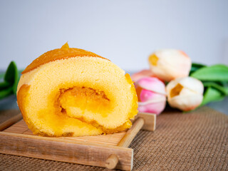 Close up of orange cake roll with slice orange fruit on wooden plate.