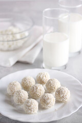 Dessert. Raffaello, cottage cheese in clear bowl, a glass of milk on a white table. Round balls in coconut chips. Background image, copy space