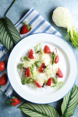 Healthy cuisine. Summer salad with fennel, strawberries, olives and herbs on a white plate on a light gray background. Delicious dishes. Restaurant menu. Rustic. Background image, copy space
