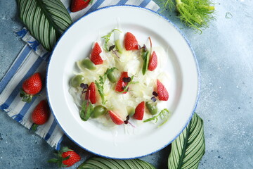 Healthy cuisine. Summer salad with fennel, strawberries, olives and herbs on a white plate on a light gray background. Delicious dishes. Restaurant menu. Rustic. Background image, copy space - obrazy, fototapety, plakaty