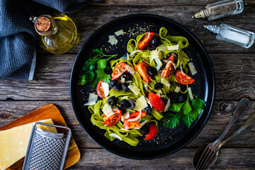 Spinach tagliatelle with parmesan, cherry tomatoes, black olives and basil on wooden table
