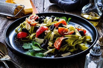Spinach tagliatelle with parmesan, cherry tomatoes, black olives and basil on wooden table
