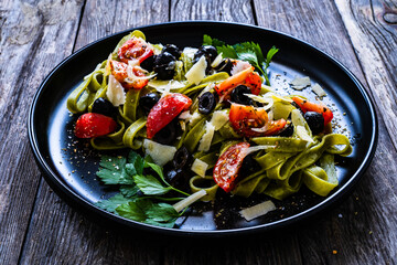 Spinach tagliatelle with parmesan, cherry tomatoes, black olives and basil on wooden table
