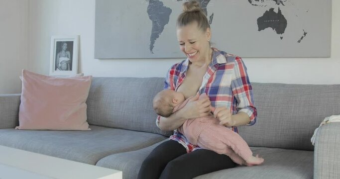 Painful Breastfeeding Of A Teething Baby. Medium Shot Of A Young Mother At Home Having Trouble Feeding Her Baby.