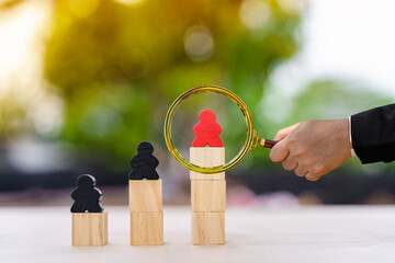 Employer hand hold a magnifier with searching for employees  with choice of a leader with red standing on the stack wooden cube is the winner of the one in the office, HR recruiting staff concept.