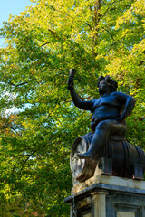 black statue of bacchus with the treetop in the background