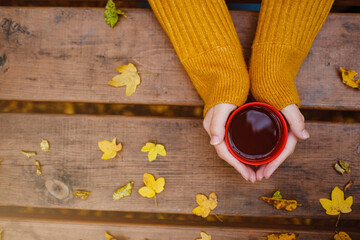 cup of hot tea in female hands holding it on wooden autumn
