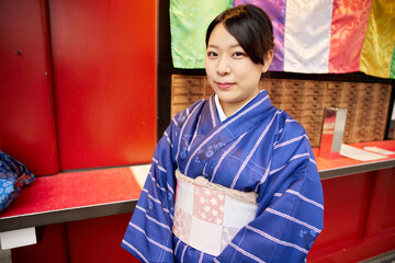 カラフルな弾幕の「おみくじ」と書かれた場所の前で微笑む着物を着た日本人女性