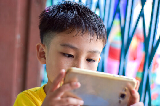 Asian child with squint eyes playing mobile game with smartphone. Concept of eye strain and screen addiction.