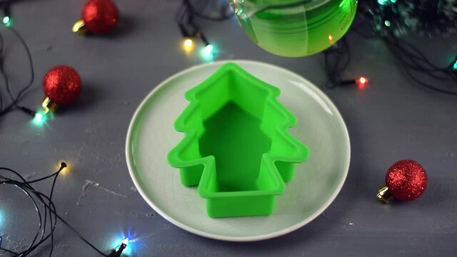 Pouring green jelly mix into the silicone mold shaped as Christmas tree. Making festive dessert