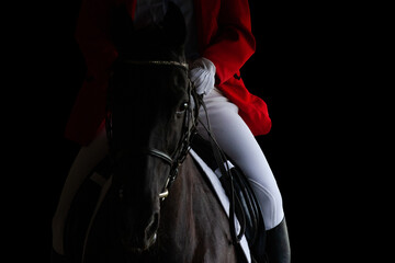 A rider in red jacket on horseback riding on dark background. Sportsman on black horse isolated on black background.