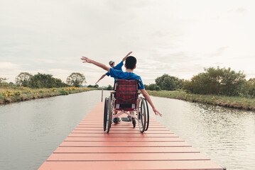 Behind of young man with disability  and father relaxing on wooden bridge jutting into the lake at...