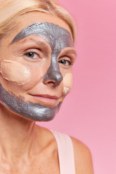 Photo of mysterious young woman applies silver beauty mask and foundation takes care of skin looks directly at camera has well cared complexion isolated over pink background. Time for beauty