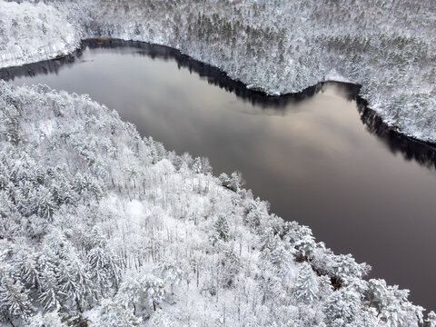 Aerial, drone photography of a lake and forest in winter season in Sweden. View from above of trees and ground covered with snow.	