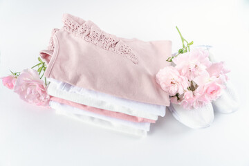 A  stack of pink and white beachwear for children on a white background. Sneakers decorated with pink flowers