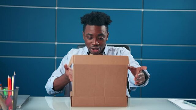 Frustrated dissatisfied African American man open cardboard box receive damaged wrong parcel. Disappointed male consumer having problem with bad fake online shop post shipping delivery order concept.