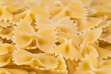 Detail of raw egg butterfly pastas on heap with beautiful blurring in background. Closeup of yellow bow-tie pasta texture. Uncooked dry farfalle with scalloped edge. Italian staple food. Healthy diet.