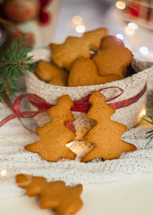 Fir tree shaped Christmas gingerbread cookies in a knitted basket near fir tree branches on a blurred background. Homemade Christmas cookies.