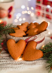 Heart shaped Christmas gingerbread cookies in a knitted basket near fir tree branches on a blurred background. Homemade Christmas cookies.