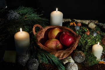 Basket with apples. Candles. Christmas balls. Pine branch, moss, wild berries, hazelnuts, cones, birch bark.