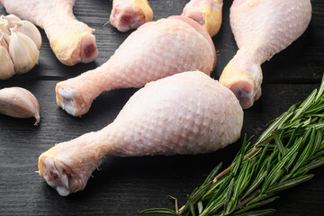 Raw uncooked chicken legs, drumsticks , with seasoning and herbs rosemary and thyme, on black wooden table background