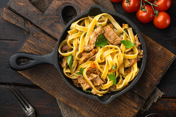 Tagliatelle with chanterelles and stewed rabbit, in frying cast iron pan or pot, on old dark ...