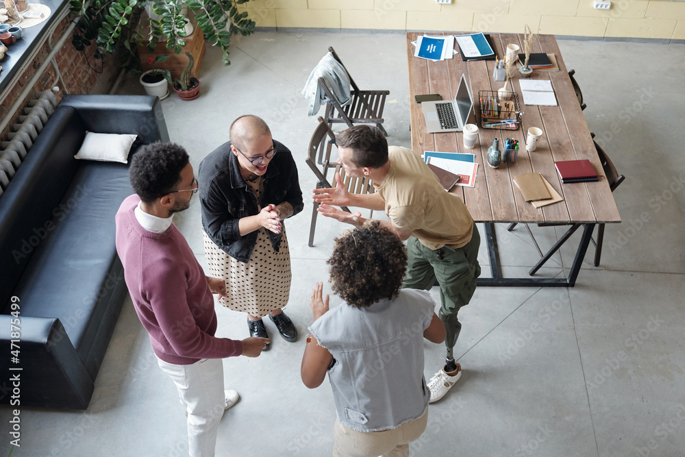 Poster Several happy young office workers having fun at break while standing in circle between black leather couch and table and playing